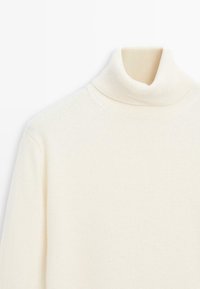 Maglione a collo alto di colore crema realizzato in morbido tessuto a maglia. Presenta un colletto alto e una texture a coste, con una finitura liscia.