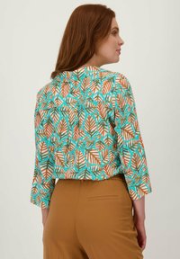 Gevoerd blouse met een tropisch bladmotief, met teal, oranje en wit op een lichte achtergrond. Inclusief driekwart mouwen en een losse pasvorm.