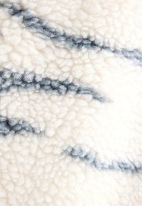 Plyšová biela tkanina s jemnou textúrou, na povrchu sú tmavomodré vlnovité čiary, ktoré vytvárajú vzorovaný efekt.