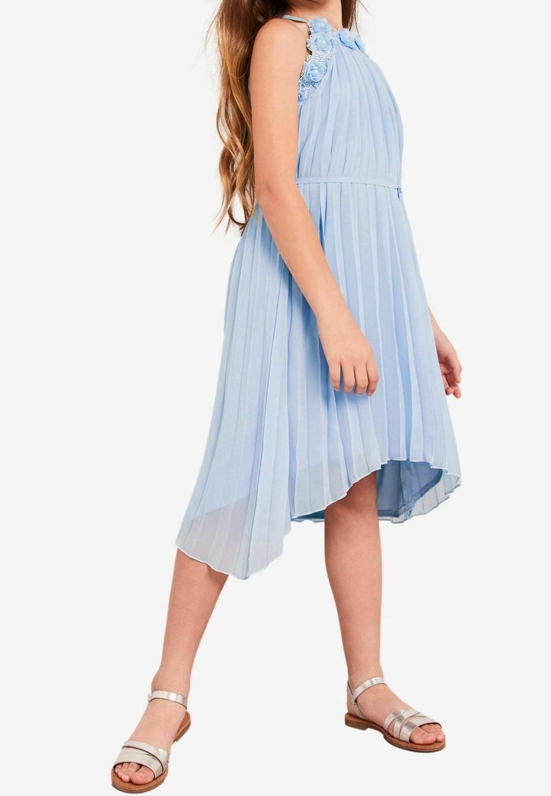 Vaaleansininen pleatattu mekko, jossa on kukkakoristeet olkapäillä, epäsymmetrinen helma ja sileä pinta; yhdistettynä hopeisiin sandaaleihin.