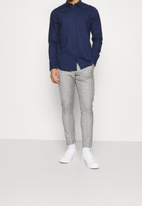 Marinblå långärmad skjorta med knappar ihop med grå rutiga slim-fit byxor och vita sneakers. Slätt tyg, åtsittande design och subtila mönster.