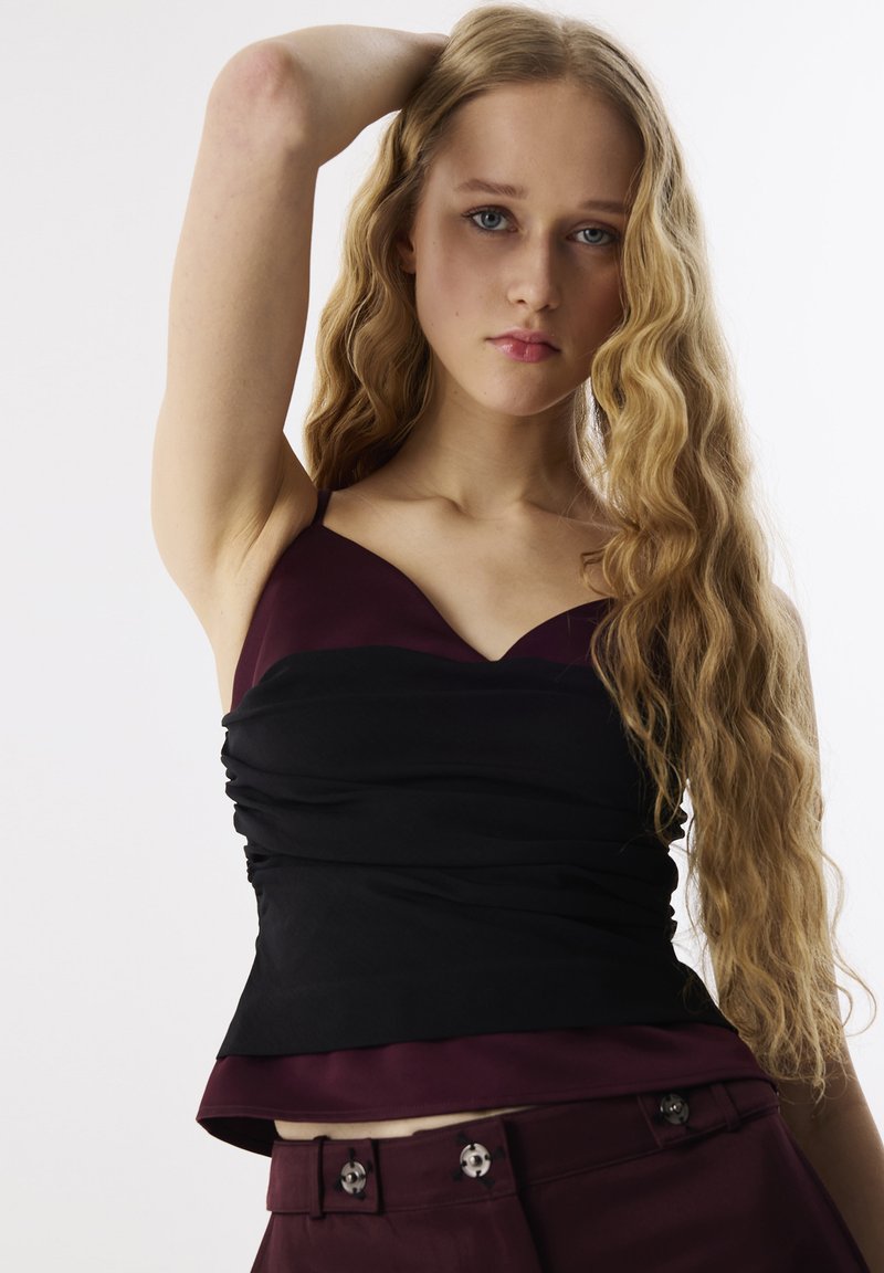 Zwarte en bordeauxmarl sleeveless top met een gerimpelde textuur en een sweetheart halslijn, gecombineerd met burgundy hoge taille broek met decoratieve knopen.