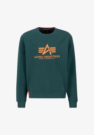 Vihreä huppari, jossa on oranssi logo "ALPHA INDUSTRIES", kolme va-horizontal -raitana, resorit hihansuissa ja pieni punainen etiketti helman kohdalla.