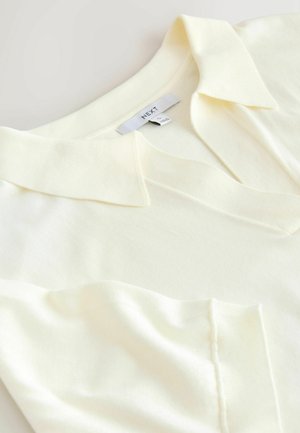 Bleg gul kortærmet poloshirt med krave, lavet af tekstureret stof og med en lille brystlomme. Brandmærke synligt.