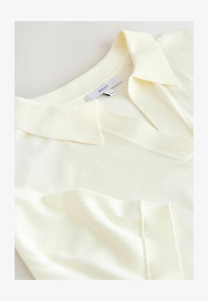 Blassgelbes kurzärmeliges Poloshirt mit kragen, aus strukturiertem Stoff und mit kleinem Brusttasche. Markenetikett sichtbar.