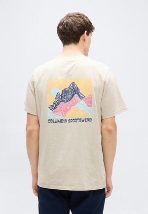 Μπεζ βαμβακερό t-shirt με πολύχρωμο γραφικό βουνού στην πλάτη και κείμενο "COLUMBIA SPORTSWEAR" κάτω από το σχέδιο.