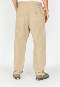 Beige cargo pants with an elastic waistband, two back pockets, and a logo patch. Fabric is sturdy with a smooth texture.