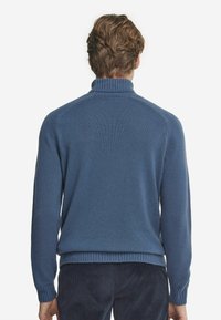 Blå, ribbad stickad tröja med hög krage och långa ärmar, med en avslappnad passform och texturerad yta vid ärmsluten och nederkanten.