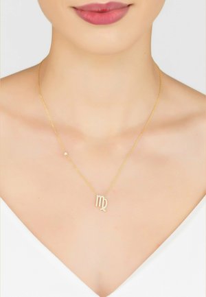 Gold necklace with a delicate chain, featuring a Virgo zodiac symbol adorned with small, shimmering stones. Simple design on a smooth neckline.