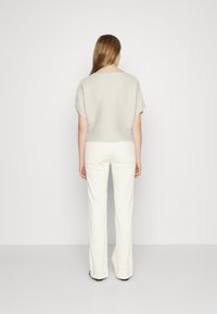 Light gray textured short-sleeve knit top paired with white flared trousers, viewed from the back. Simple design and relaxed fit.