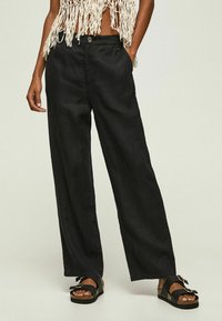 Czarne spodnie szerokie wykonane z lekkiego materiału, z zapięciem na guzik i dwoma bocznymi kieszeniami. Połączone z płaskimi czarnymi sandałami.