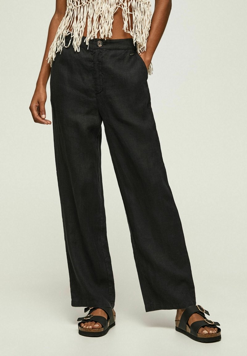 Czarne spodnie szerokie wykonane z lekkiego materiału, z zapięciem na guzik i dwoma bocznymi kieszeniami. Połączone z płaskimi czarnymi sandałami.