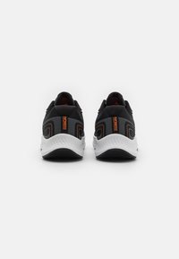 Zapatos deportivos negros con suela blanca, con acentos en naranja, parte superior de malla texturizada y un cuello acolchado para mayor comodidad.