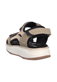 Sandali beige e neri con design aperto, dotati di cinturini in Velcro, perforazioni e una suola bianca spessa con battistrada marrone strutturato.