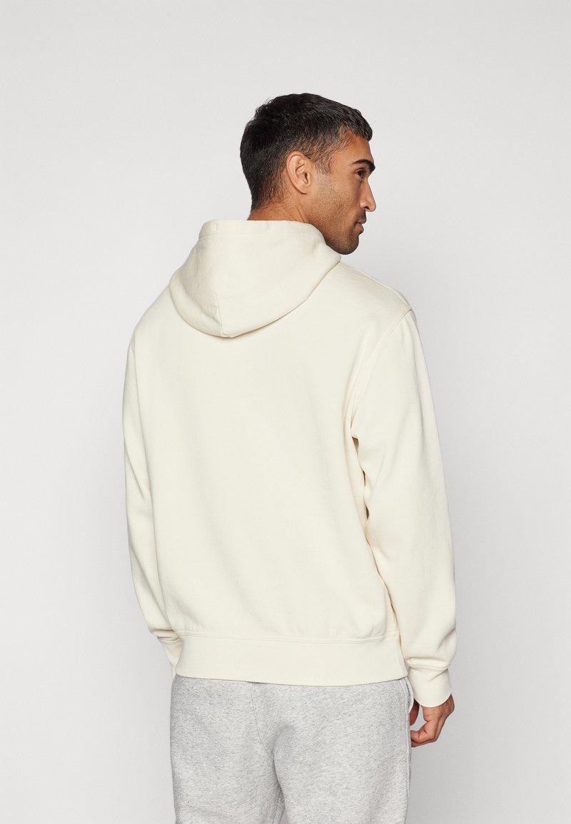 Sudadera crema con capucha ajustable, puños acanalados y cinturilla, textura suave, con un diseño simple sin gráficos ni logotipos.