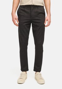 Mørke ternede bukser med en tætsiddende pasform, der har en glat tekstur og sidelommer, kombineret med lyse sneakers.