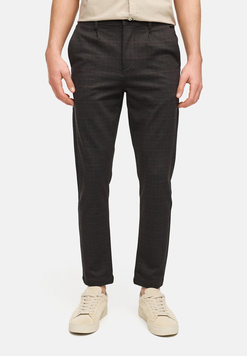 Mørke ternede bukser med en tætsiddende pasform, der har en glat tekstur og sidelommer, kombineret med lyse sneakers.