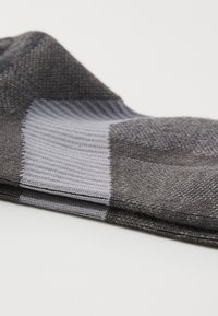 Calcetines grises con un patrón texturizado, puño acanalado y un diseño de bloques de color con secciones de gris claro y gris oscuro. Tejido suave.