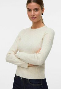 Cremfarbener, gerippter Langarm-Strickpullover mit Rundhalsausschnitt, der aus einem strukturierten Stoff besteht und eine taillierte Silhouette hat, kombiniert mit dunklen Jeans.