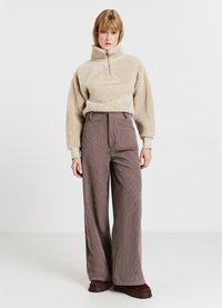 Pullover in pile beige con cerniera a quarto giro abbinato a pantaloni a gamba larga in velluto a coste marrone con tasche frontali e tessuto strutturato.