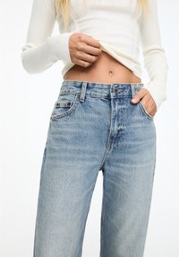 Jeans de mezclilla azul claro con cintura alta, pierna recta y costuras visibles. Ajustados en la cintura, con bolsillos frontales y un botón de metal.