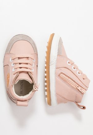 Zapatillas altas de cuero rosa con suelas blancas y grips de goma. Características incluyen detalles en ante, cordones y una cremallera lateral para un acceso fácil.