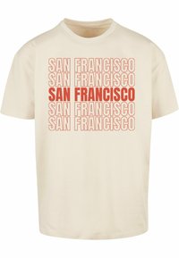 Krémové bavlnené tričko s opakovaným textom "SAN FRANCISCO" v tučnom a normálnom písmene, striedajúce červené a tmavšie červené odtiene.