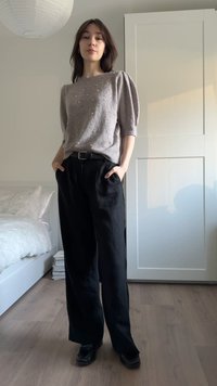 Lysegrå strikket sweater med pufsleeves og perle-accenter, kombineret med sorte højhændede bukser med vide ben og sorte sko.