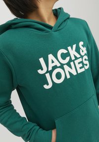 Zelena kapuca iz mehkega materiala z velikim belim logotipom "JACK & JONES", sprednjim žepom in kapuco na zavezovanje.