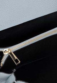 Borsa a mano in pelle azzurro chiaro con un risvolto strutturato, zip dorata e interno in tessuto nero. Caratterizzata da una chiusura con zip singola e linee pulite.