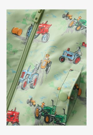 Gaiši zaļa auduma virsma ar krāsainām traktoru ilustrācijām sarkanā, zilā un zaļā krāsā, ar rāvējslēdzēju un piespraudes pogu detaļām.