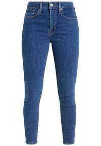 Vaqueros ajustados de mezclilla azul media, de talle alto con trabillas para cinturón, cierre frontal con botones y textura sutil desgastada en las piernas.