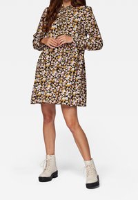 Vestito nero floreale con motivi rosa e gialli, vita arricciata e maniche lunghe. Abbinato a stivaletti alla caviglia beige con lacci.