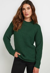 Groene gebreide trui met een geribbelde structuur, ronde hals en lange mouwen. Gecombineerd met zwarte broek met een ontspannen pasvorm.