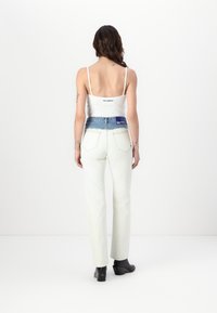 Top branco sem mangas e jeans de algodão creme de cintura alta com um cós de denim azul, combinados com botas pretas de salto. Design minimalista, textura suave.