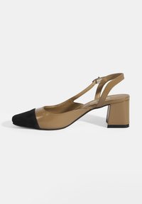 Beige and black slingback shoe with a block heel. Features glossy leather and soft suede, pointed toe, and a cut-out design with ankle strap.