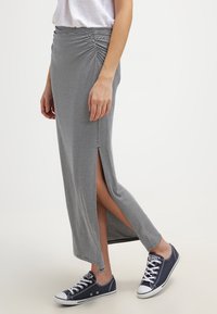 Jupe maxi rayée grise et blanche avec des fentes latérales et un détail froncé à la taille, associée à des baskets bleu marine décontractées.