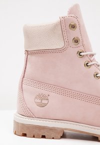 Bottine en cuir rose avec col rembourré, œillets en métal, lacets blancs, semelle en caoutchouc et logo d'arbre embossé sur le talon.