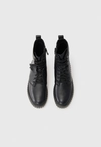 Bottines en cuir noir avec une finition texturée, présentant un design à lacets, une fermeture éclair latérale et une semelle en caoutchouc épaisse et à points.
