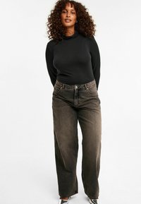 Schwarzes Langarmtop kombiniert mit weit geschnittenen, ausgebleichten braunen Jeans, die über vordere Taschen und einen Knopfverschluss verfügen. Einfaches, lässiges Design.