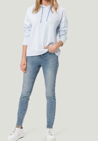 Un hoodie bleu clair avec une coupe ample, des manches longues et un cordon de serrage. Associé à un jean skinny en denim clair et des sneakers blanches.