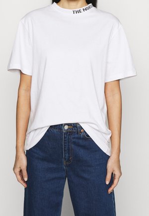 Person wearing a plain white t-shirt with "THE NORTH" visible on the collar, paired with high-waisted dark blue jeans.