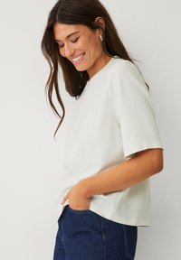 Haut blanc à manches courtes avec un col rond, en tissu lisse, associé à un jean bleu foncé. Texture subtile, coupe décontractée.