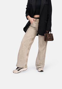Jean large beige avec une texture délavée, associé à un top noir court et un blazer oversized noir, accentué par un sac à main en imprimé léopard.