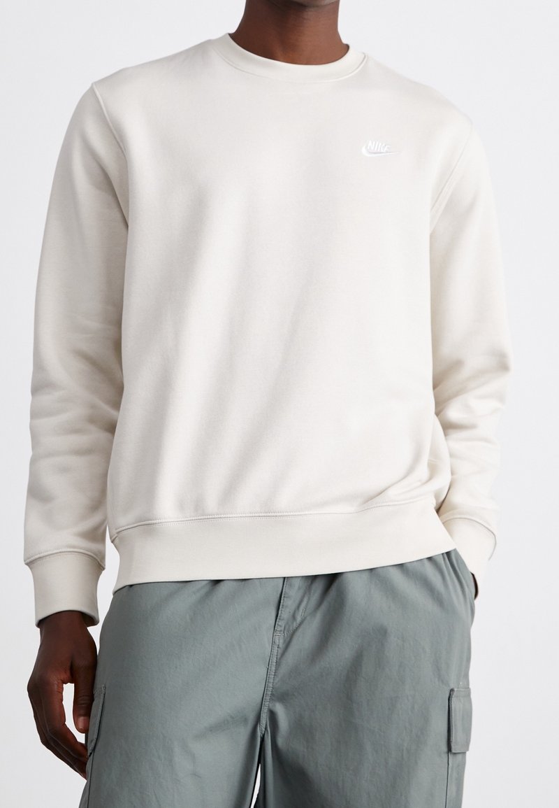 Light beige sweatshirt with a round neck and ribbed cuffs. Features a small white Nike logo on the chest. Pairing with tailored green cargo pants.