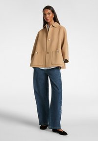 Beige ullkappa med krage och silverknappar, med två främre fickor. I par med vida mörkblå jeans och svarta ballerinas.