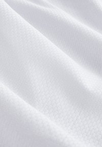 Tissu blanc avec une texture subtile en nid d'abeille et des plis doux, montrant une surface textile lisse et légère.