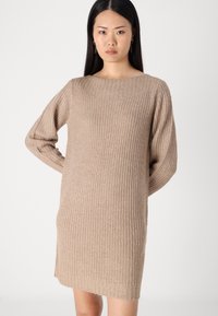 Robe pull en tricot beige avec des manches longues, texture côtelée et encolure ronde. Légèrement plus courte d'un côté, avec une coupe décontractée.