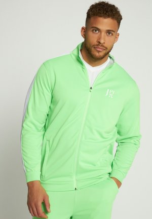 Groene sportjack met volledige rits, witte zijstrepen en een logo op de borst. Gemaakt van gladde, rekbare stof.