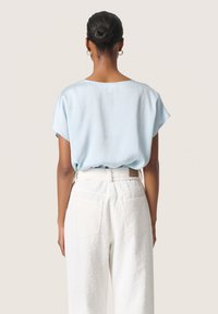 Top azzurro chiaro a maniche corte con vestibilità comoda, realizzato in tessuto testurizzato e con scollatura rotonda, abbinato a pantaloni bianchi testurizzati e una cintura.